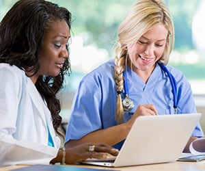 Doctor and nurse look at a laptop smiling,