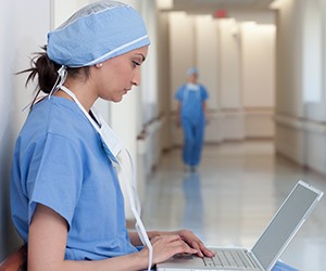 Nurse typing on laptop in hospital hallway.